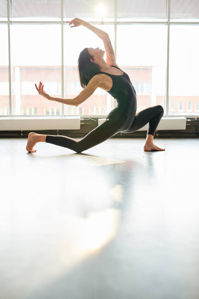 Full length portrait of contemporary young woman dancing passionately in studio hall lit by serene sunlight, copy space - Photo, Image