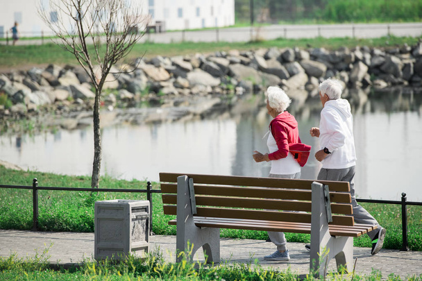 Side view portrait of active senior couple running in park along lake, copy space - Valokuva, kuva