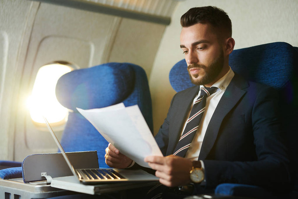 Portret van knappe bebaarde zakenman werken terwijl u geniet van de vlucht in eerste klas, kopieer ruimte - Foto, afbeelding
