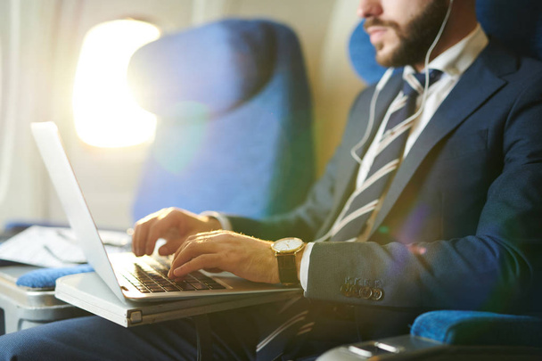 Porträt eines nicht wiederzuerkennenden Geschäftsmannes, der auf der Tastatur tippt, während er den Laptop während des First-Class-Fluges im Flugzeug benutzt, Kopierraum - Foto, Bild