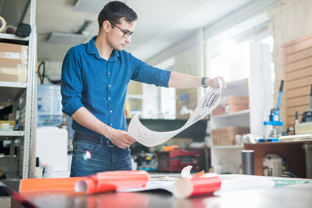 Casual man in glasses holding paper placard while working in modern office of typography - 写真・画像