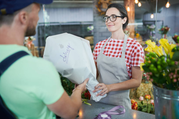 Portrait of beautiful woman handing bouquet to delivery man in flower shop - Photo, Image