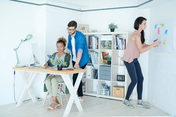 Full length portrait of group of modern designers working in small white office, focus on African-American woman sitting at desk, copy space - Valokuva, kuva