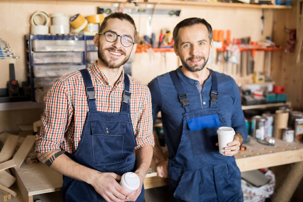 Retrato de cintura hacia arriba de dos carpinteros sonrientes mirando a la cámara mientras descansan en el trabajo
 - Foto, imagen