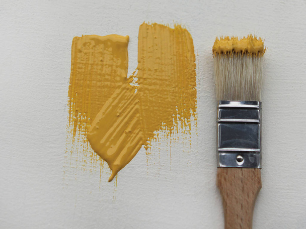 A small paint brush with yellow paint lies on a white surface with fresh yellow paint strokes. - Foto, immagini