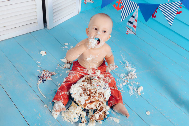decoration for the boys birthday, smash the cake in a nautical marine style. stylized birthday ship photo shoot. Cheerful boy eats and break a cake with his hands on the first holiday - Foto, afbeelding