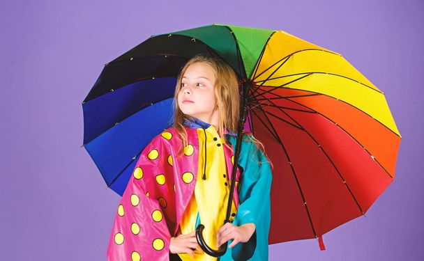 Kid girl happy hold colorful umbrella wear waterproof cloak. Waterproof accessories for children. Enjoy rainy weather with proper garments. Waterproof accessories make rainy day cheerful and pleasant - Fotó, kép
