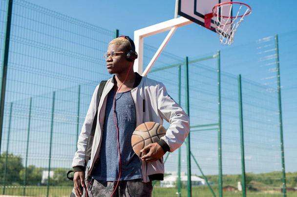 コートに立つバスケットボールボールを持つ現代アフリカ人男性のウエストアップ肖像画、コピースペース - 写真・画像