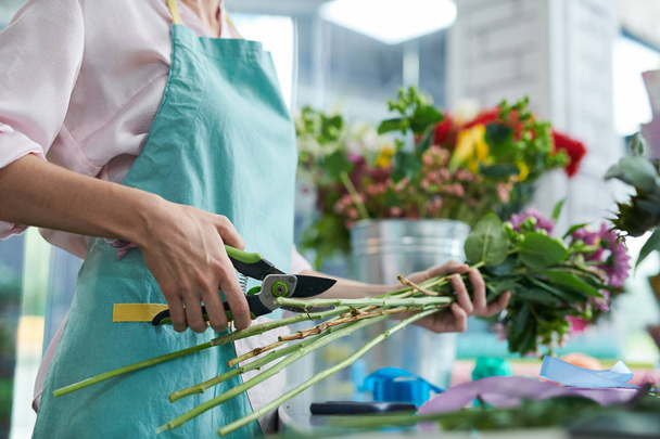 Retrato de sección media de florista femenina irreconocible cortando tallos en flores mientras arregla ramos en la tienda, espacio para copiar
 - Foto, imagen