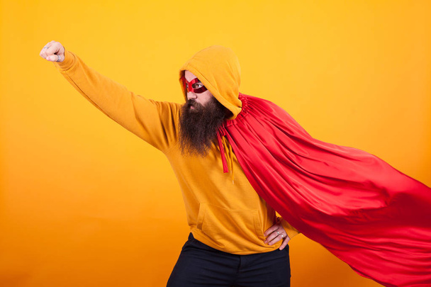 Супергерой в красной накидке и маске улетает в студии на жёлтом фоне
 - Фото, изображение