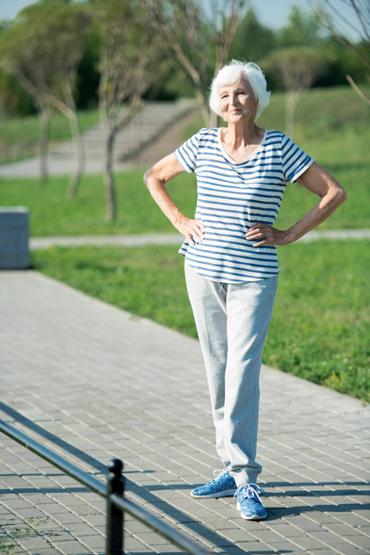Full length portrait of cheerful active pensioner posing outdoors standing o running track in park, copy space - Photo, Image