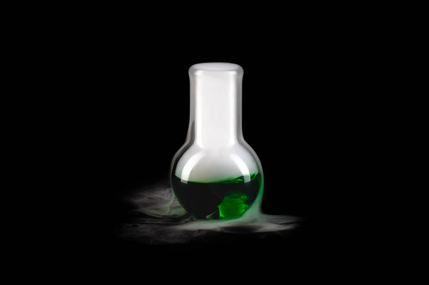 Close up of glass flask with green steaming liquid on black background, copy space - Φωτογραφία, εικόνα
