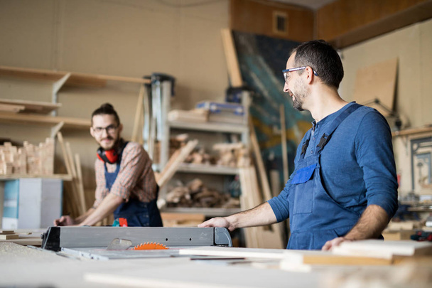 Retrato de dos carpinteros alegres mirándose mientras trabajan en carpintería, espacio para copiar
 - Foto, imagen