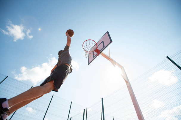 Широкоугольный портрет молодого спортсмена, стреляющего слэм-данк на баскетбольной площадке на открытом воздухе, копировальное пространство
 - Фото, изображение