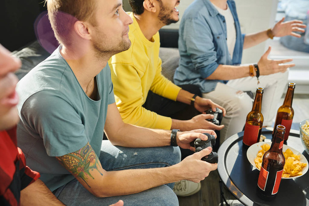ジョイスティックでソファに座り、自宅でビデオゲームで友人と遊ぶ集中した若者 - 写真・画像