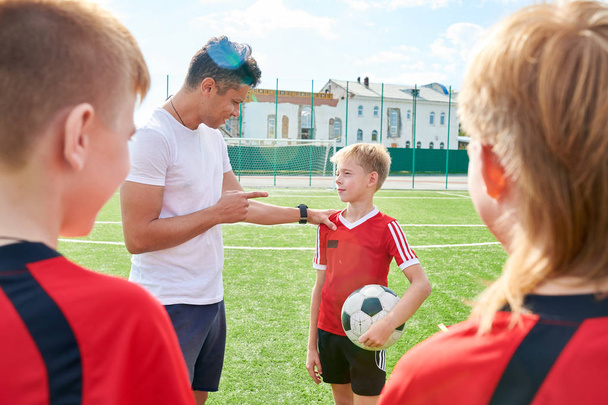 Portret boku uśmiechniętego trenera rozmawia z juniorskim zespołem piłki nożnej dając instrukcje przed meczem - Zdjęcie, obraz