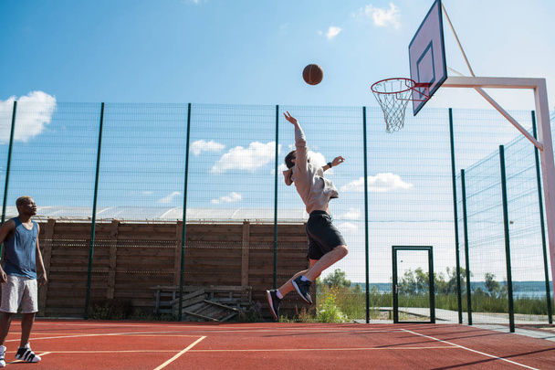 Wide angle side view of young sportsman jumping high and shooting ball in hoop caught in mid air, copy space - Fotografie, Obrázek