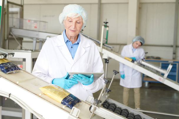 Portret starszych kobiet kontrolujących proces produkcyjny w nowoczesnej fabryce żywności i patrząc na torby makaronu przesuwne w dół przenośnika taśmowego, przestrzeń kopiowania - Zdjęcie, obraz