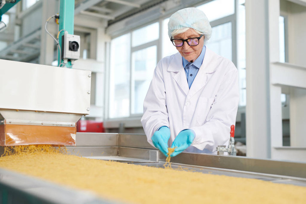 Portrait d'une femme âgée travaillant à l'usine et inspectant la production alimentaire sur bande transporteuse de macaronis, espace de copie
 - Photo, image