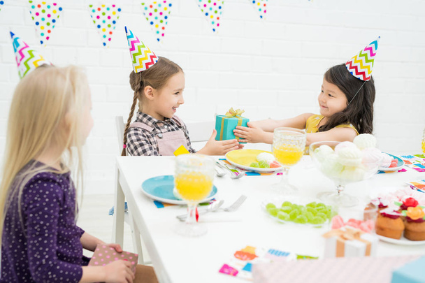Inhalt attraktive asiatische Mädchen mit lockigem Haar sitzt am Tisch und Geschenk an Geburtstagskind bei der Feier - Foto, Bild