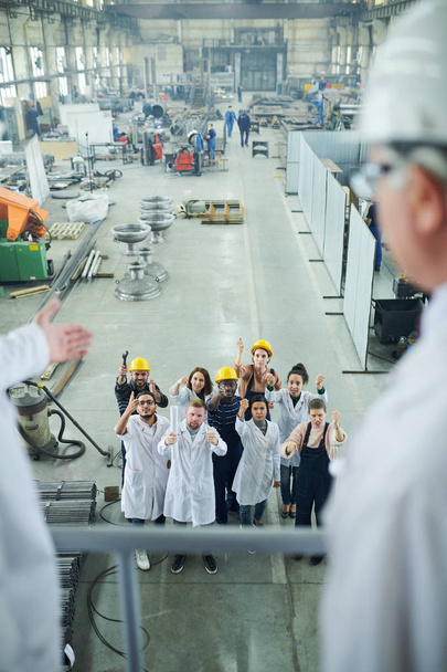 Προβολή υψηλής γωνίας σε πολυεθνική ομάδα εργαζομένων που διαμαρτύρονται κατά τη διάρκεια της απεργίας, εξετάζοντας δύο διευθυντές εργοστασίου που στέκονται στο μπαλκόνι, αντιγράψτε το χώρο - Φωτογραφία, εικόνα