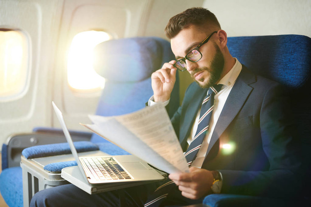 Side view portrait  of handsome bearded businessman reading document and working while enjoying flight in first class, copy space - Photo, Image