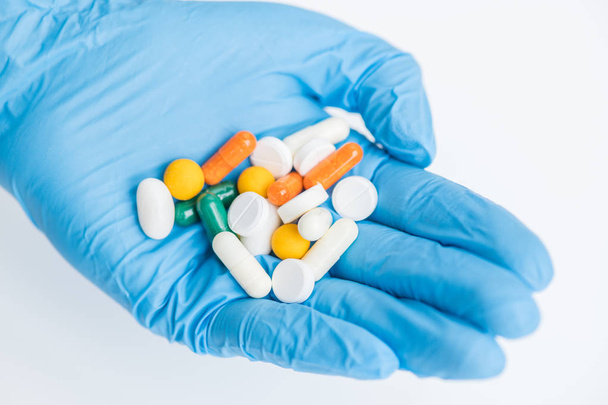 Lähikuva käsine kädessä tilalla valikoituja pillereitä yli valkoinen tausta, lääketiede ja hoito käsite
 - Valokuva, kuva