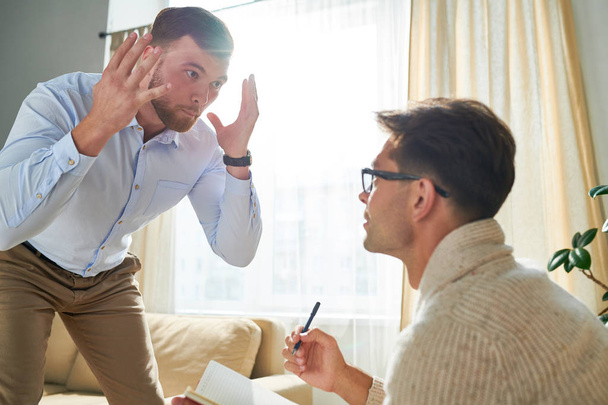 Psikiyatrist ile randevuda duygularını ifade ederken sakallı duygusal genç adam el sallıyor - Fotoğraf, Görsel