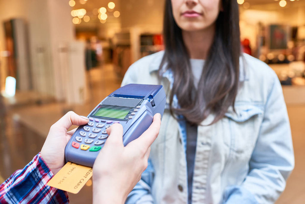 Молодая женщина использует свою кредитную карту, чтобы заплатить за покупку в магазине
 - Фото, изображение