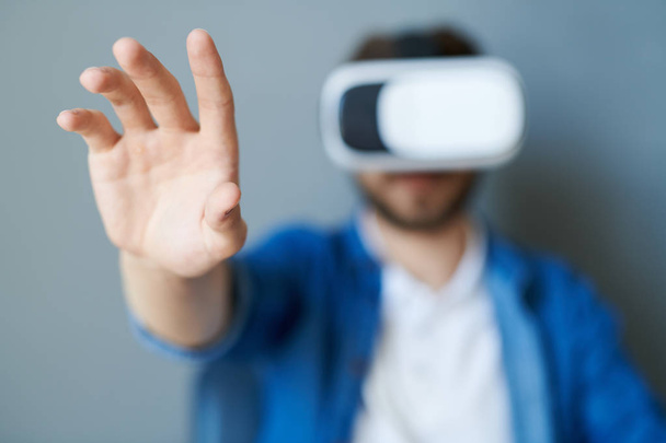 Ritratto di giovane uomo moderno con attrezzatura VR seduto in poltrona che tende la mano mentre gioca o guarda 360 video, copia lo spazio, concentrati sul primo piano
 - Foto, immagini