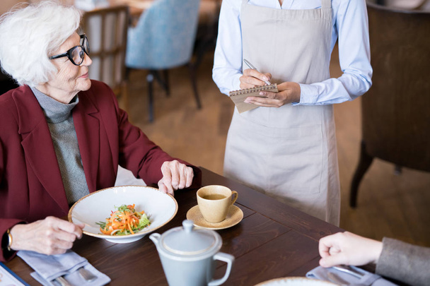 Donna anziana seduta al ristorante con insalata sul tavolo e fare un ordine per il suo vicino
 - Foto, immagini
