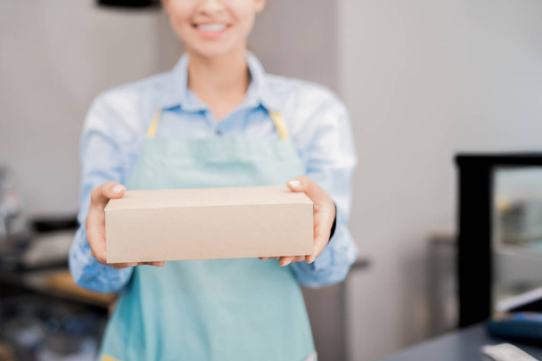 Keskiosa muotokuva tunnistamaton nainen yllään esiliina tilalla laatikko takeaway ruokaa ja hymyillen onneksi, kopioi tilaa
 - Valokuva, kuva