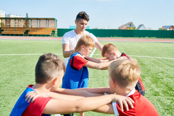 Full length portrait of PE teacher helping boys doing warm up exercises on grass outdoors, copy space - Photo, image
