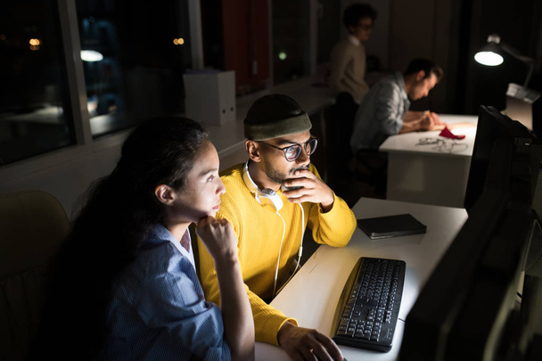 Portrait de plusieurs personnes travaillant dans un bureau sombre la nuit, mettant l'accent sur deux collègues utilisant l'ordinateur au premier plan, espace de copie
 - Photo, image