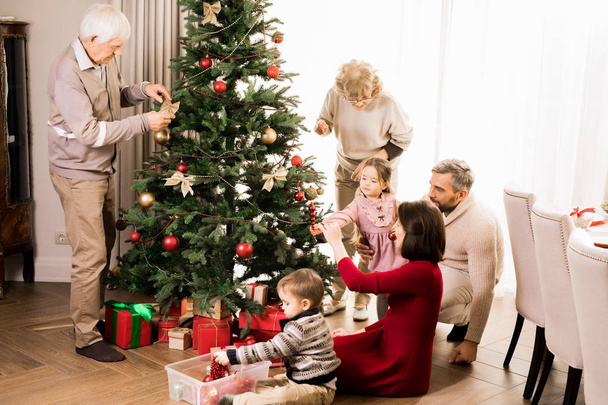 İki sevimli çocuk ve dedesi ile Noel ağacı dekorasyon büyük mutlu aile sıcak tonda tam uzunlukta portre, kopya alanı - Fotoğraf, Görsel