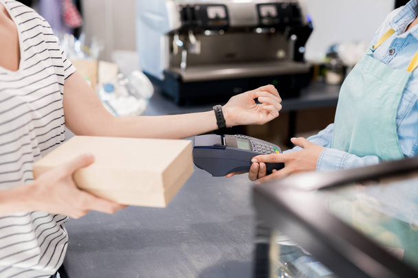 Вид сбоку, где неузнаваемая женщина платит через NFC умными часами за свой заказ в кафе
 - Фото, изображение