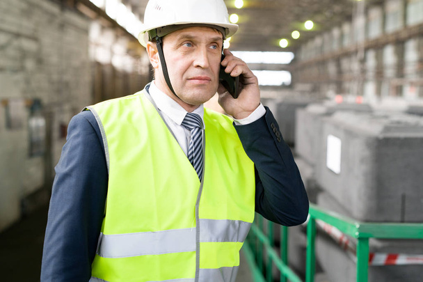 Waist up portrait of mature businessman wearing hardhat speaking by phone during factory inspection - Fotoğraf, Görsel