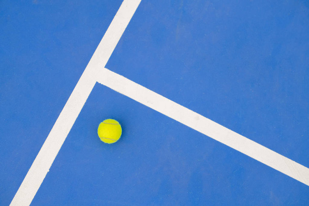 Graphic sports background of yellow tennis ball laying on blue floor in court, copy space - Фото, изображение