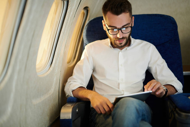 Portrait of handsome bearded man using digital tablet while enjoying first class flight by sunset, copy space - Photo, image