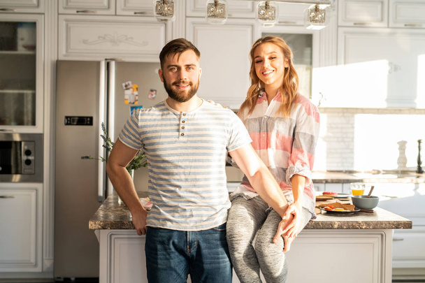 Portrait de couple heureux moderne posant à la maison et regardant la caméra tout en restant debout dans la cuisine
 - Photo, image