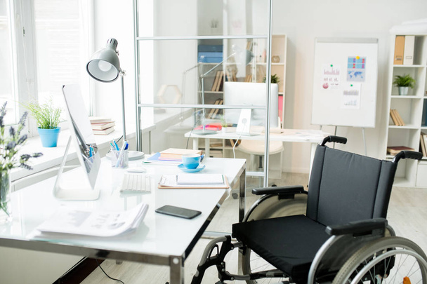 Nowoczesne miejsce pracy biurowej z dokumentami i monitorem komputerowym i wózkiem inwalidzkim przy stole - Zdjęcie, obraz