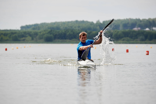 Ο αθλητής κρατάει ένα κουπί και επιπλέει στη λίμνη. - Φωτογραφία, εικόνα
