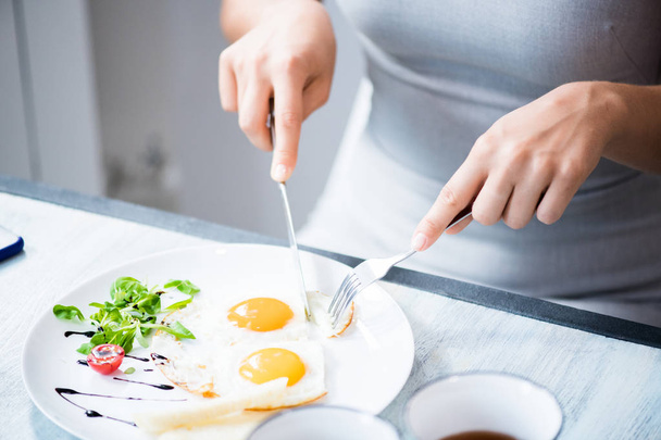 Closeup of unrecognizable young woman cutting beautiful fried egg dish while enjoying healthy breakfast in cafe, copy space - Фото, изображение