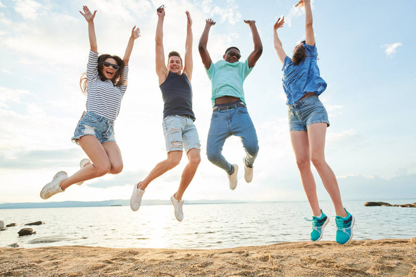 Jovens amigos se divertindo na praia e pulando contra o belo lago
 - Foto, Imagem