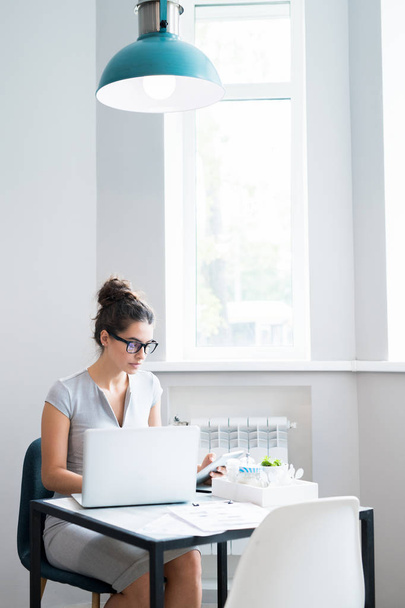 Портрет красивой молодой женщины в очках, сидящей одна за столом в кафе за окном и пользующейся ноутбуком, копировальным пространством
 - Фото, изображение