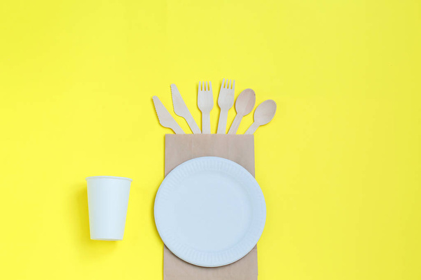 Eco-friendly disposable utensils made of bamboo wood on paper bag on yellow background. - Photo, Image