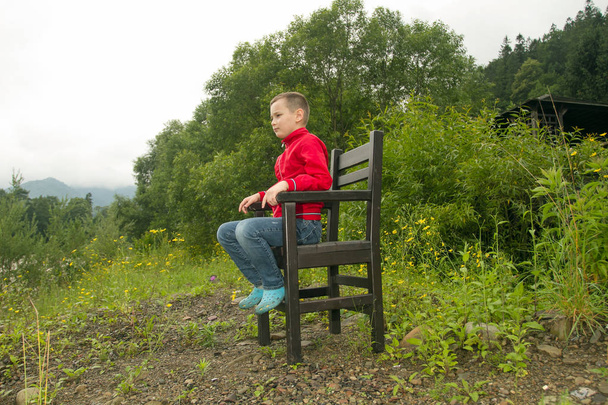 Jongen zit op stoel in het bos - Foto, afbeelding