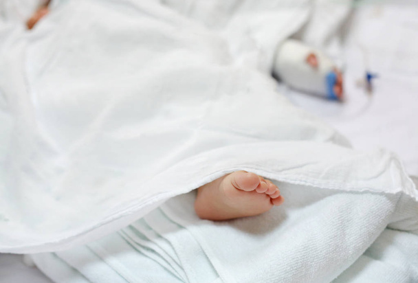 Close up patient baby feet sleep on bed at hospital with blur Saline intravenous drip on baby hand. - Photo, image