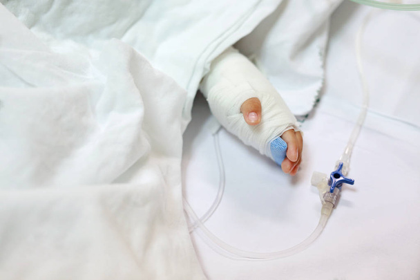 Close up baby hand on patient's bed in hospital with saline intravenous. Baby admitted at hospital. Kid patients have IV tube. - Foto, Bild