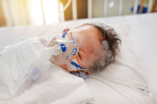 Inhalation baby boy age about 1 years old on patient bed. Respiratory Syncytial Virus (RSV). Intensive care on bed at hospital. - Фото, изображение